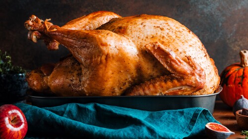 Roasted whole turkey on a table surrounded by an apple, a pumpkin, and figs for the family Thanksgiving Holiday/